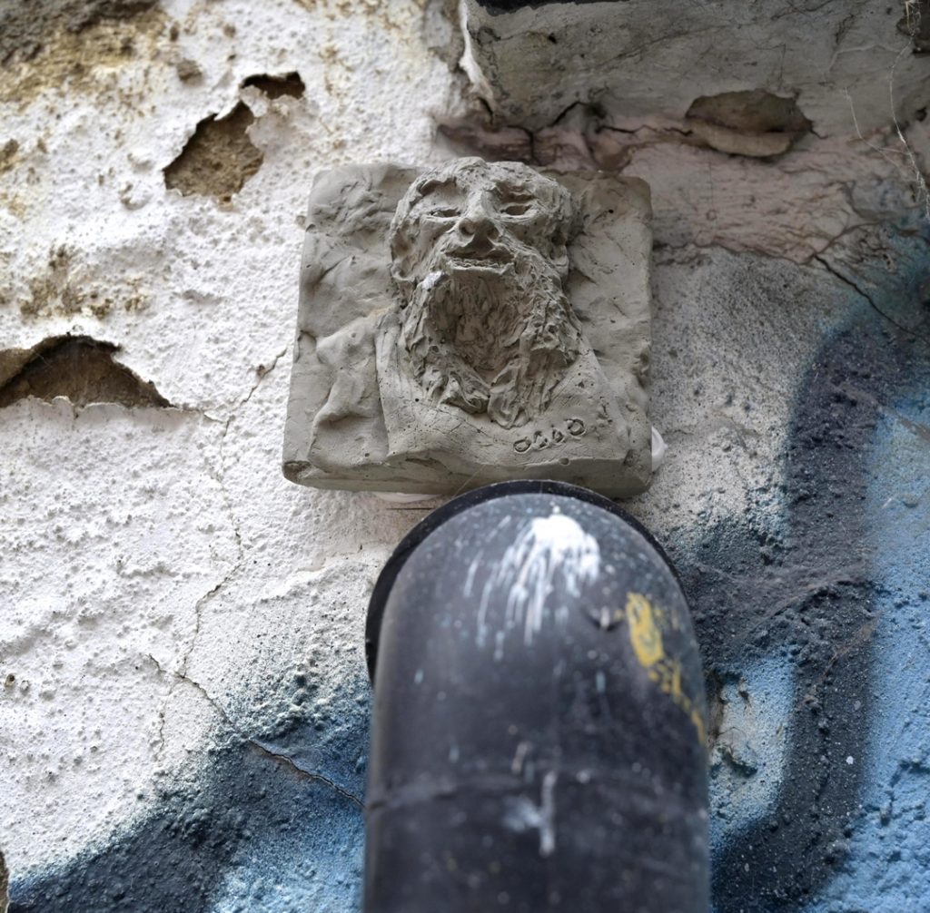 Miniature plaque shoing a bearded face in relief mounted on an outdoor wall with cracked paint