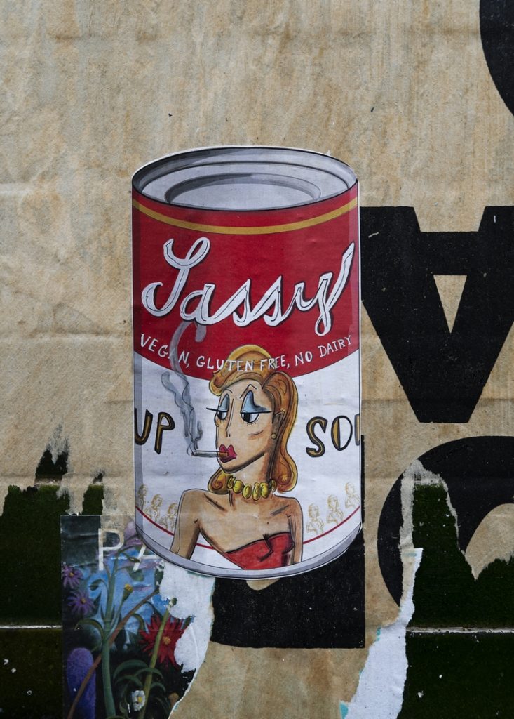 paste up street art showing a cartoon of a Campbells Soup Tin with a Sassy Lady smoking a cigarette