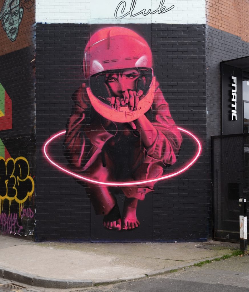 neon pink girl wearing motor bike helment crouches in a circle of neon light by David Speed in Shoreditch