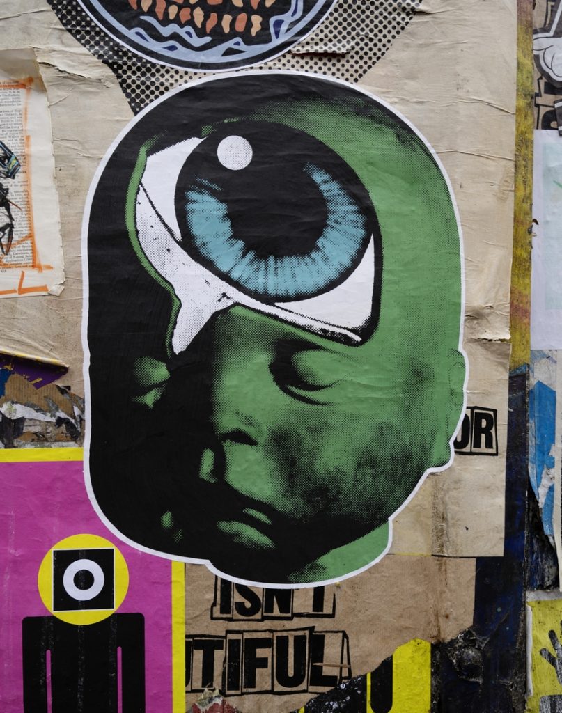 paste up street art by Paul Insect showing a green baby face with a huge eye in its head called a Baby head